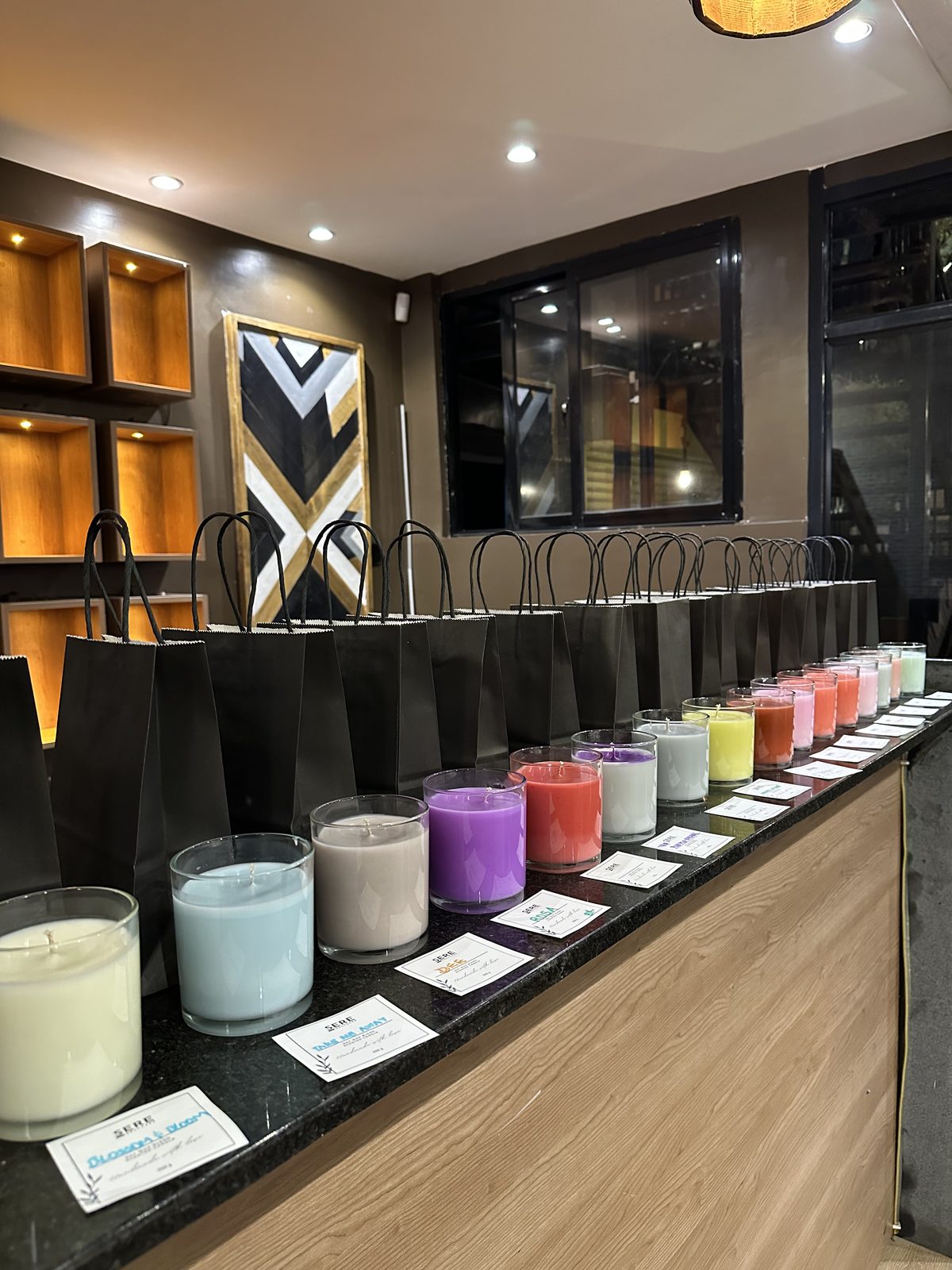 A row of colourful Sere candles in front of black Sere gift bags